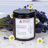 Premium soy wax candle made with local lavender essential oil by brigid trading company lavender chamomile candle for aromatherapy bed time, scents the air naturally gifts for sleep and relaxation hand made by brigid trading company kitsap county Washington state made in usa picture shows countertop with soy wax candle in a jar, lavender and chamomile flowers for detail 7 ounce amber jar candle